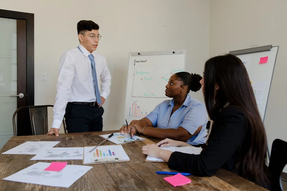 A diverse group of professionals collaborating around a table with charts and laptops.